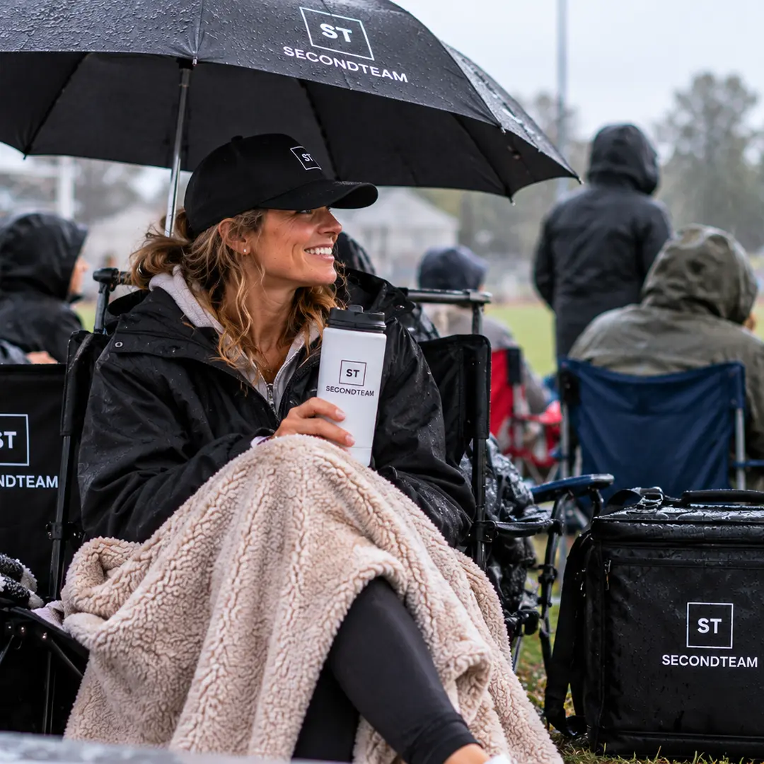 Parent smiling under a SECONDTEAM umbrella on a rainy game day