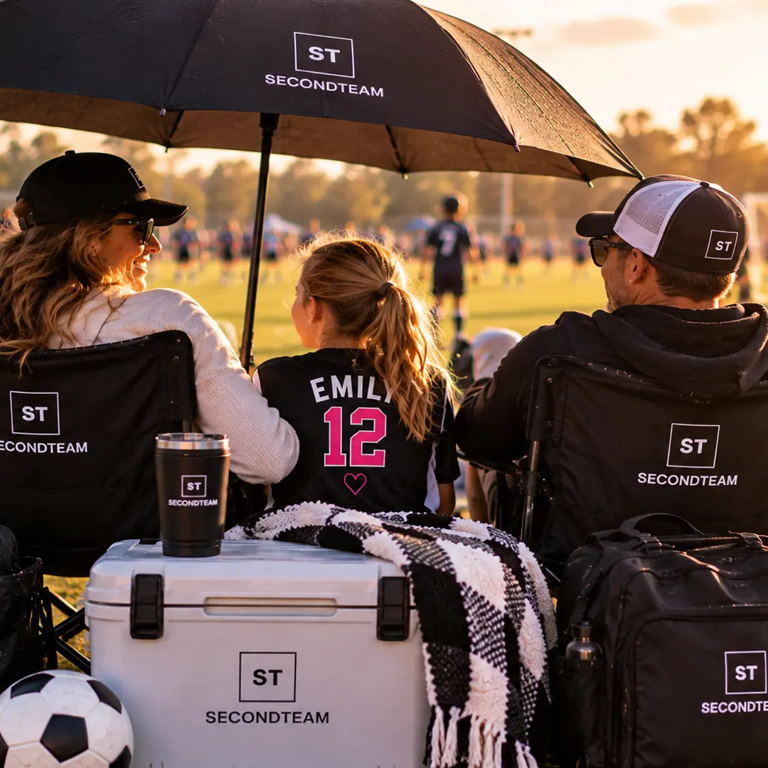 Family watching from SECONDTEAM chairs under an umbrella at golden hour