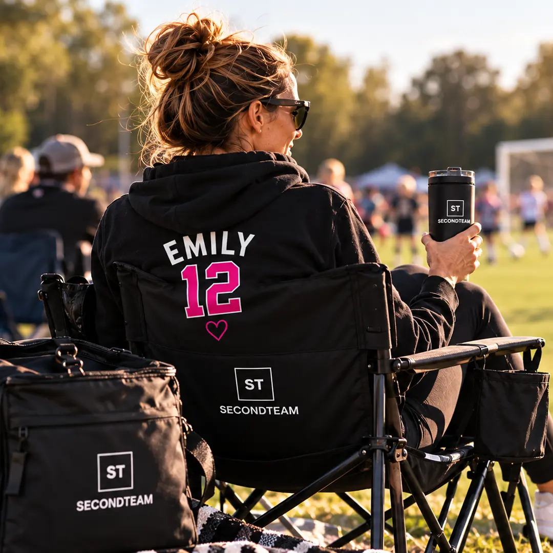 Parent in an EMILY 12 hoodie cheering from a sideline chair